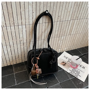 Detail of black tote bag with white stitching, heart charm and fringe tassel decor
