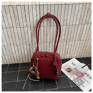 Detail of burgundy suede tote bag featuring white contrast stitching and bag charms