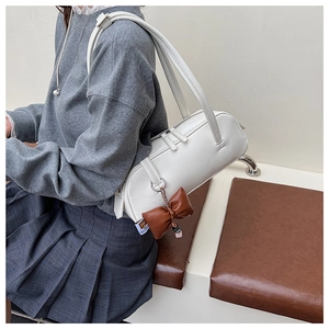 Détail du sac baguette blanc cylindrique avec un élégant charme de nœud marron foncé