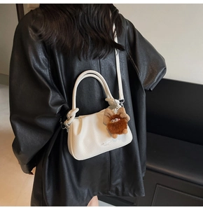 Close-up of white lychee textured shoulder bag with a brown plush monster charm on the side