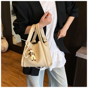 Dettaglio della borsa a secchiello beige con trama litchi, ciondolo scimmia e perle