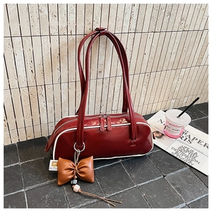 Détail du sac baguette rouge foncé avec passepoil blanc contrasté et breloque nœud