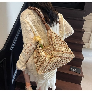 Detail of woven straw tote bag featuring brown leather ruched handles and mesh texture