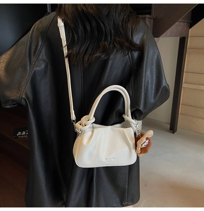 Detail of white lychee leather handbag with pleated design and brown plush monster charm