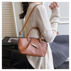 Detail of caramel leather pleated handbag featuring unique knotted handle and silver metal bar