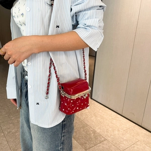 Detail view of red quilted mini crossbody bag with white beads on striped shirt