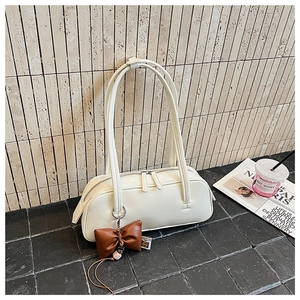 Détail d'un sac baguette blanc minimaliste avec un charm noeud en cuir marron et zip