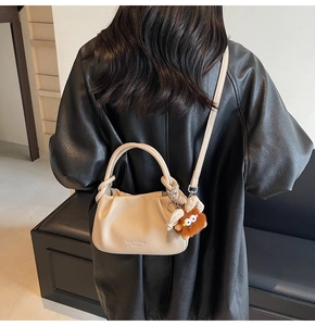 Detail of cream pleated leather crossbody bag with a brown plush charm on a model
