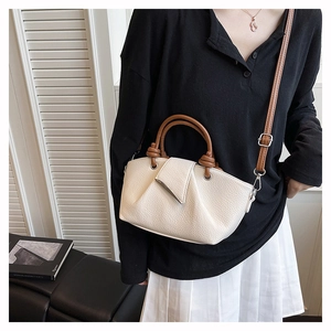 Detail of white lychee leather bag featuring a brown circular handle and adjustable strap
