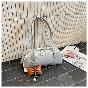 Détail du sac baguette cylindrique en cuir gris avec double fermeture éclair et breloques
