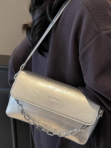 Silver metallic baguette bag with chain strap and crinkled texture worn as underarm bag