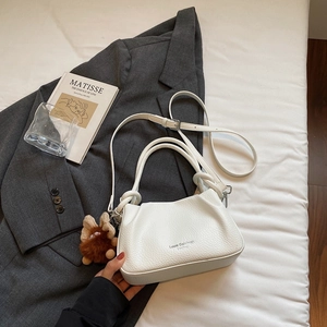 Close-up of white lychee leather handbag with brand logo and brown plush animal charm