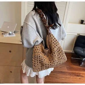 Detail of a woven straw shoulder bag with a brown ruched handle and hollow diamond pattern