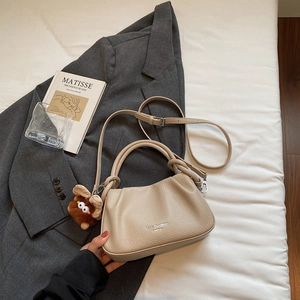 Detail of off-white pleated crossbody bag with plush monster charm on white bedding