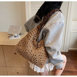 Detail of hollow woven straw tote bag with brown pleated leather shoulder strap