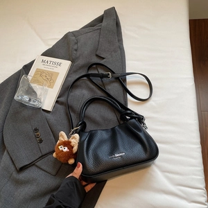 Detail of black pleated leather crossbody bag with logo and cute plush charm accessory