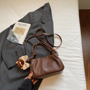Close-up of brown pebbled leather cloud bag with plush bear charm and adjustable strap