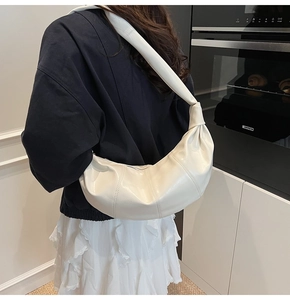 Detail view of cream white pleated hobo bag with knotted strap on a person's shoulder