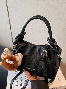 Elegant black grained leather shoulder bag with plush charm on a minimalist background