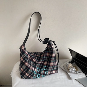 Détail d'un grand sac à carreaux avec broderie bleue posé près d'un ordinateur portable