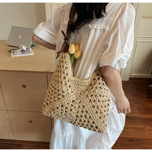 Detail of hand-woven straw tote bag featuring leather shoulder strap and knot decoration