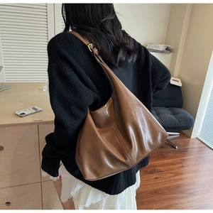 Brown leather large capacity hobo bag worn by model in a modern indoor setting