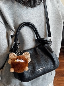 Fashionable black pebble leather crossbody phone bag with a plush charm and metal details