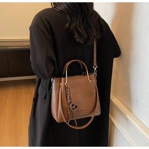 Deep brown tote bag with metal handles and fashion engraving shown on a model