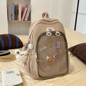 Detail of beige nylon backpack featuring a clear PVC window with cute charms and badges