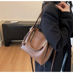 Brown leather tote with metal handles and woven charm shown in a lifestyle street setting