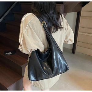 Detail of glossy black hobo bag with adjustable gold metal buckle on shoulder strap