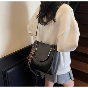 Detail of black leather bucket bag featuring gold handles and heart tassel charm on model