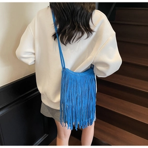 Detailed view of a blue suede crossbody bag featuring long tassels and slim shoulder strap