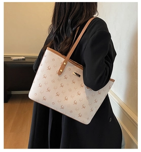 Detail einer schicken cremefarbenen Monogramm-Tasche mit braunen Ledergriffen am Modell