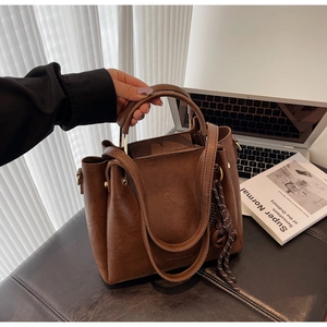 Detail of brown leather tote bag with braided lanyard shown in a workspace scene