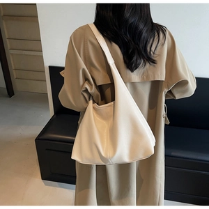Chic beige large capacity hobo tote bag worn with a stylish trench coat in an indoor setting