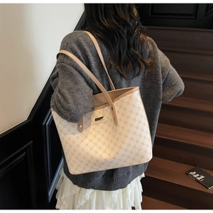 Vista lifestyle di una grande borsa tote crema con motivo monogramma marrone a spalla