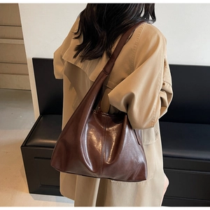 Detail of glossy coffee leather tote showing the wide strap and soft texture on a trench coat