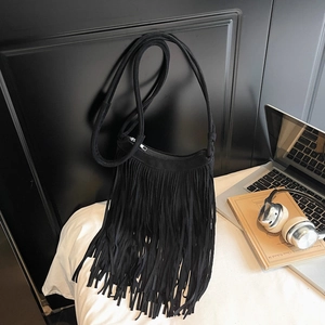 Detail of black suede shoulder bag featuring long fringe tassels and a bohemian style