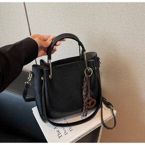 Detail of black textured tote bag with golden hardware and pretzel bag charm
