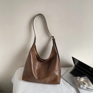Detail of a large brown leather hobo bag next to a laptop in an office setting