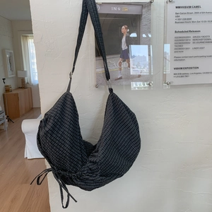 Détail du sac besace à carreaux bleus avec cordons de serrage sur un mur texturé blanc