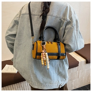 Detail of a mustard Boston bag with black straps and decorative wooden beads on a handle