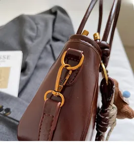 Dettaglio macro della borsa in pelle marrone scuro con ganci dorati e ciondolo a orso