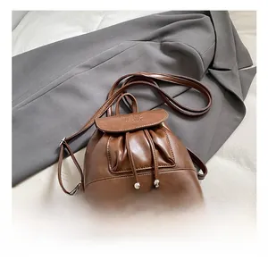 Detail view of brown PU leather bucket backpack with drawstring and metal ball pendants