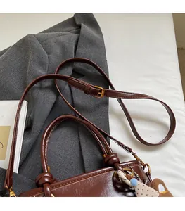 Dettaglio della tracolla regolabile e fibbia dorata su una borsa a secchiello marrone