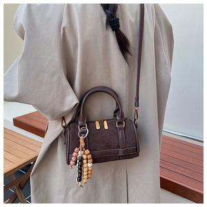 Detailed view of a retro brown Boston bag with wooden bead charm and suede leather texture