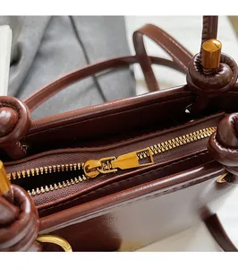 Dettaglio della cerniera dorata e del manico annodato di una borsa in pelle marrone
