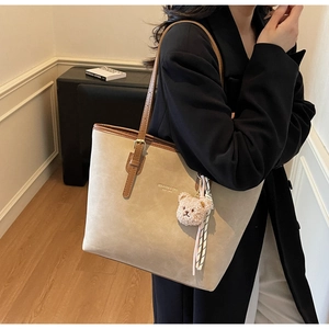 Detail of beige suede tote bag with brown leather straps and pink bear charm decoration