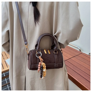 Detailed view of a dark brown suede Boston bag with leather straps and beaded charm